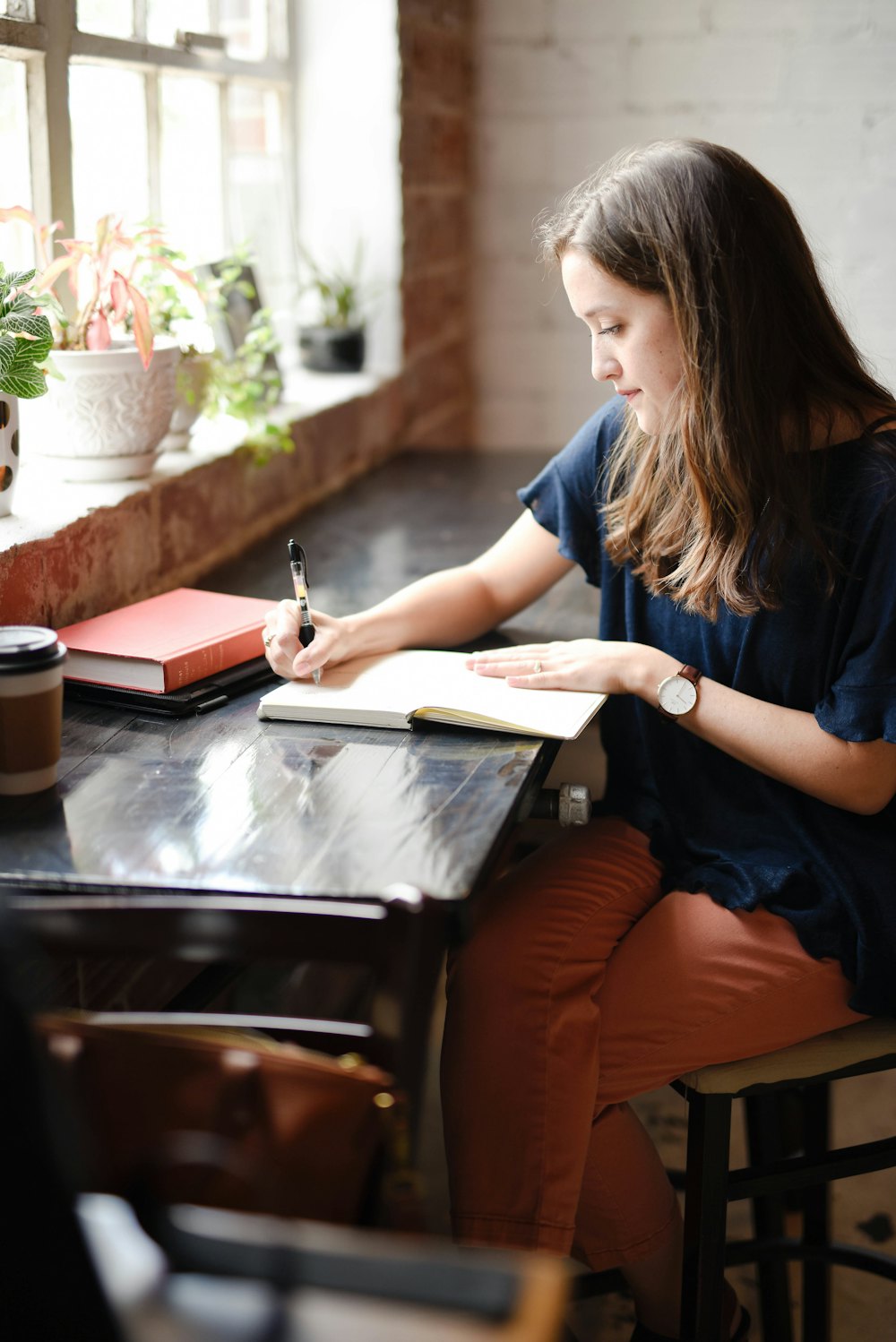 A student writing by hand in a notebook at a sunlit desk